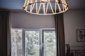 A room with a large window, curtains, a hanging light fixture, and a framed picture on the wall.