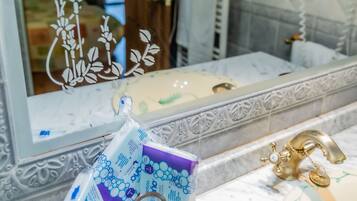 Un baño con lavamanos de mármol, grifo dorado y espejo con un adhesivo floral decorativo. Una cesta de mimbre con artículos de tocador está sobre el mostrador.