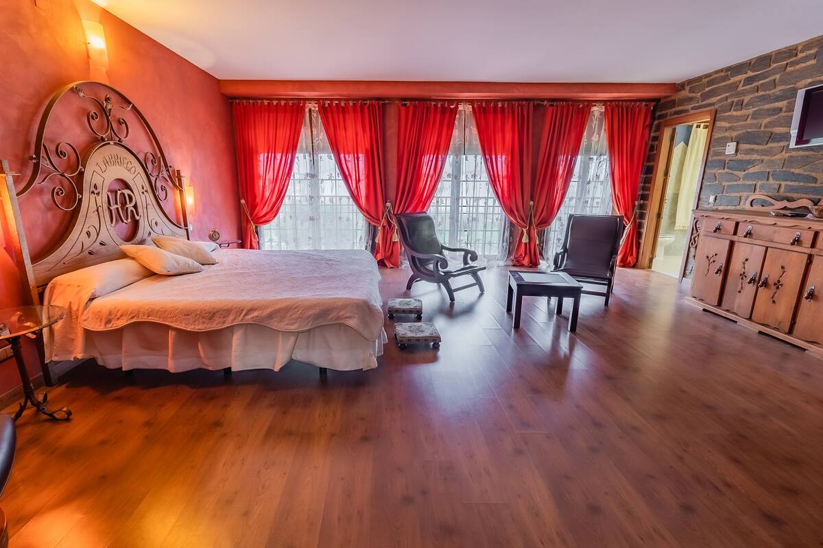 A bedroom with a large bed, a chair, a small table, and a wooden cabinet.