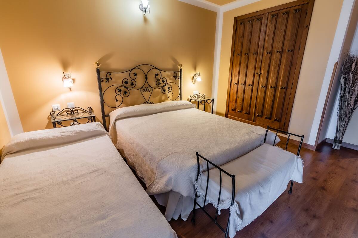 A room with two beds, a wooden wardrobe, and two bedside tables with lamps.
