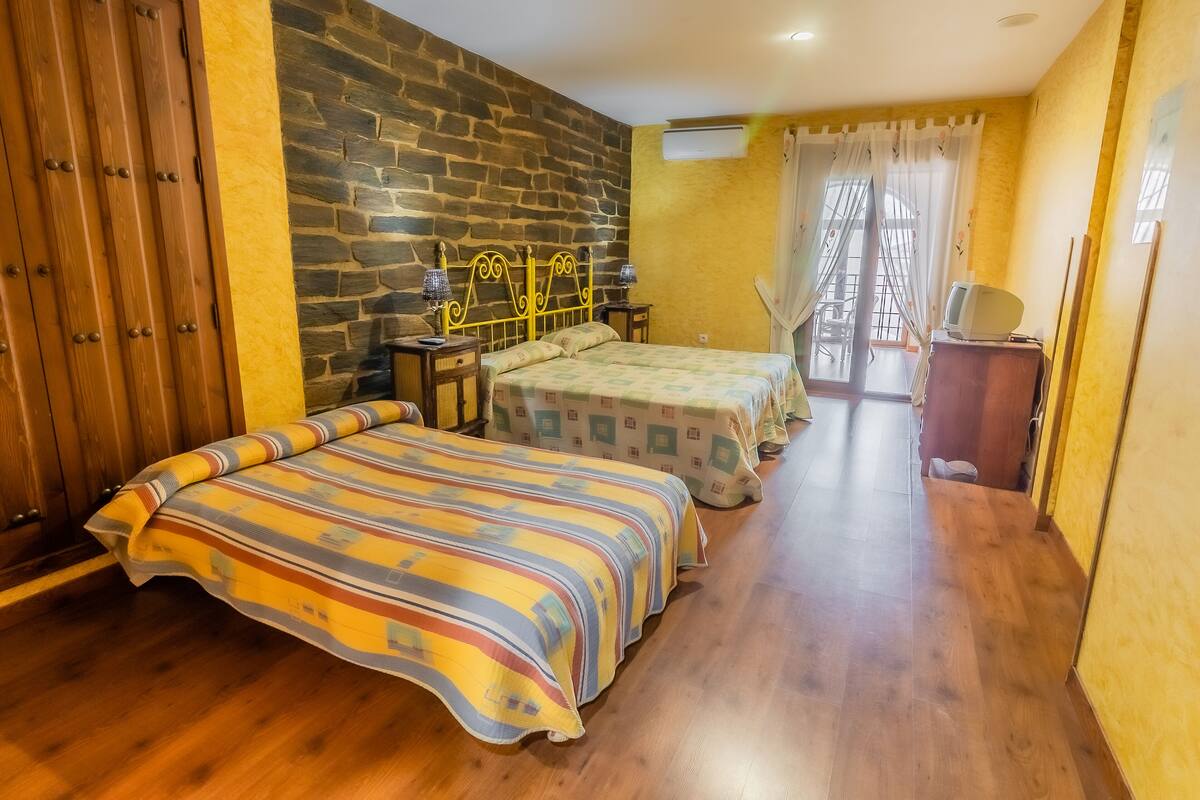 A bedroom with two beds, a stone wall, wooden flooring, a TV, and a window with curtains.