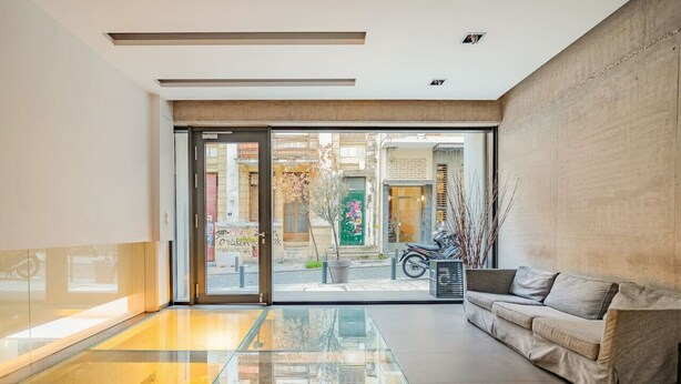 A modern interior with a glass floor leading to an outdoor area, a sofa, and a concrete wall. - Modern Oasis Build on Acropolis Ruins Free Parking (Athina)