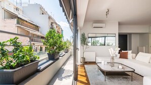 A modern apartment with a balcony, a white sofa, a coffee table, and potted plants. - Modern Oasis Build on Acropolis Ruins Free Parking (Athina)