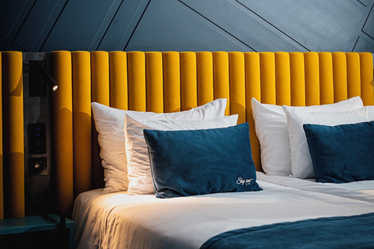 Ett modernt hotellrum med en säng, en sänggavel med vertikala paneler och ett sluttande tak.