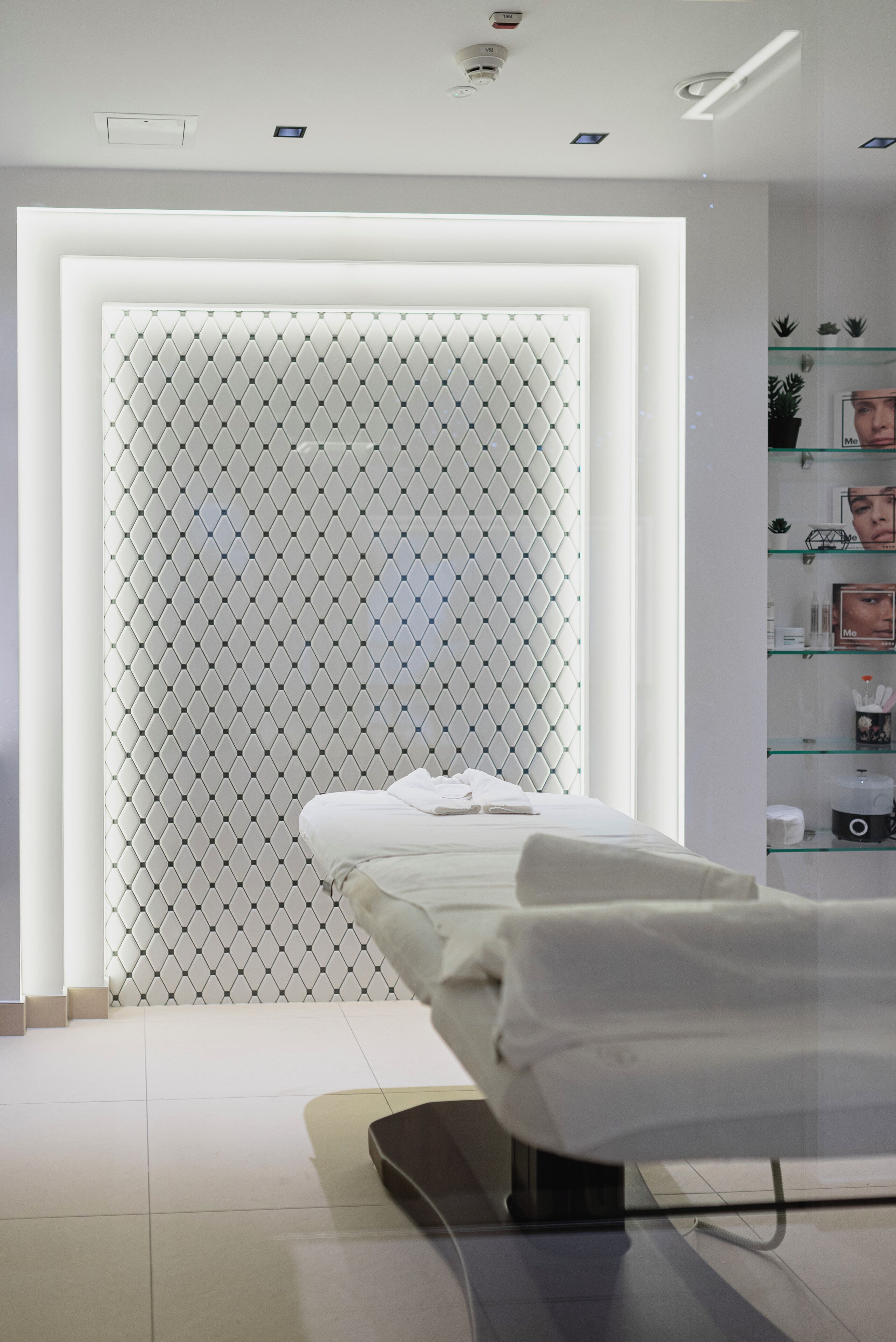 A modern, clean room with a bed, a glass display case with toiletries, and a patterned wall.