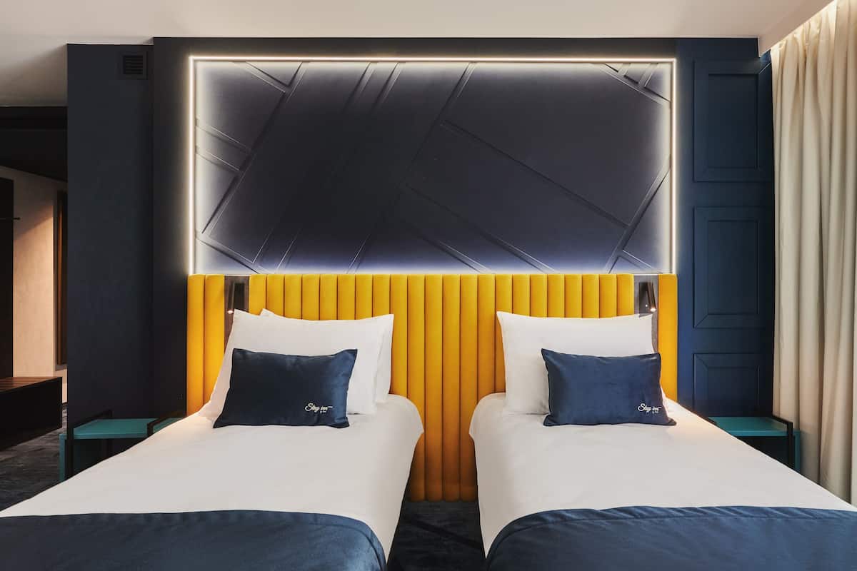 Ett hotellrum med två sängar, en modern sänggavel och ett nattduksbord med en lampa.