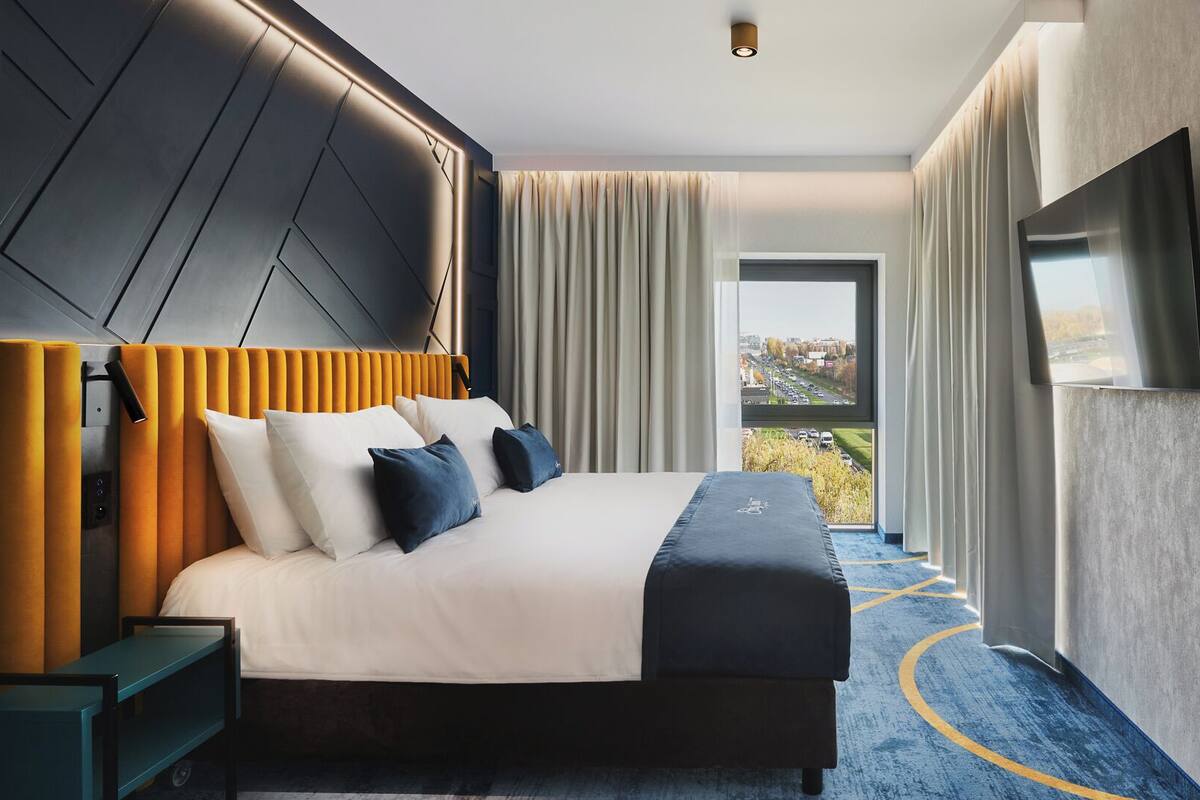 Ett modernt hotellrum med en stor säng, en tv på väggen och utsikt över staden genom fönstret.