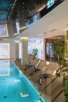 A modern indoor pool area with lounge chairs and a glass door entrance.