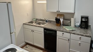 A compact kitchen with white cabinets, a dishwasher, a toaster, and a coffee maker.