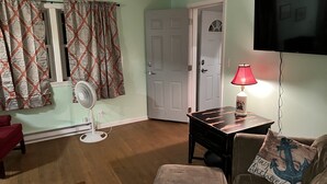 A living room with a wooden floor, a red couch, a black table, a lamp, and a TV mounted on the wall.