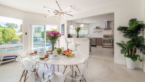 A modern kitchen with a dining area, featuring a marble table, clear chairs, and a central light fixture.