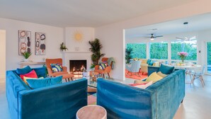A spacious living room with a fireplace, blue sofas, and a dining area with large windows.