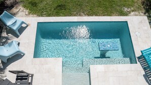 Een zwembad met helder water, omringd door een betegeld zonnedek en houten ligstoelen.