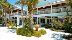 Een strandhotel met meerdere balkons, palmbomen en een bord voor Olive Oil Outpost.