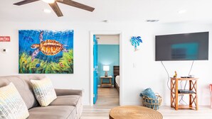 Een woonkamer met een bank, een rond houten bijzettafeltje, een televisie en een schilderij van een zeeschildpad.