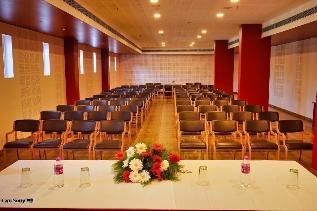 Une salle de conférence avec des rangées de chaises, une longue table agrémentée d’un arrangement floral et un écran de projection fixé au mur.