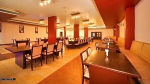 Un comedor amplio con múltiples mesas y sillas, techos altos con iluminación empotrada y una paleta de colores cálida.