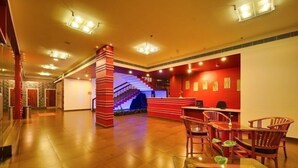 Un vestíbulo de hotel con mostrador de recepción, una escalera y una zona de estar con sillas de madera y una mesa de vidrio.
