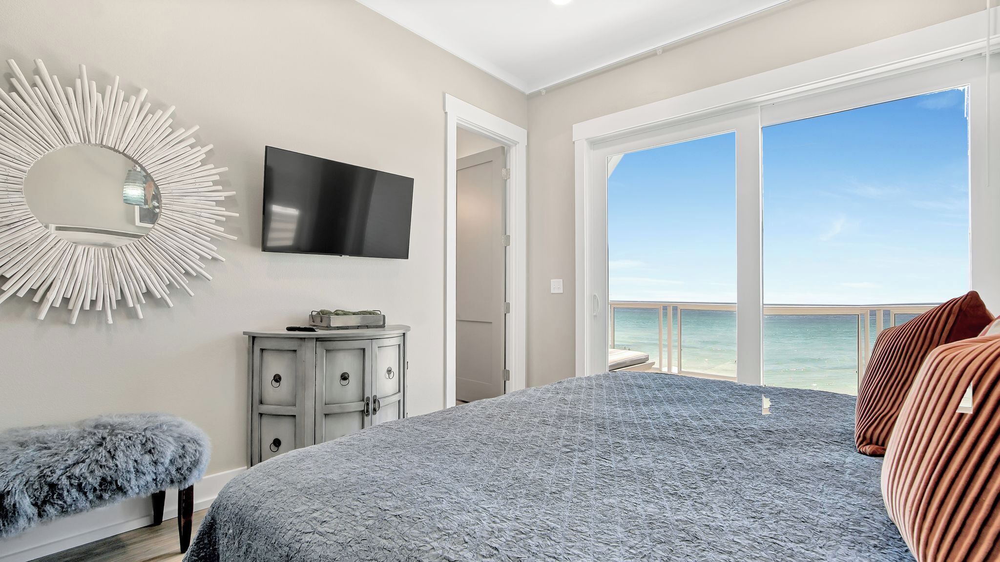 A bedroom with a large bed, a TV, a dresser, and a view of the ocean.