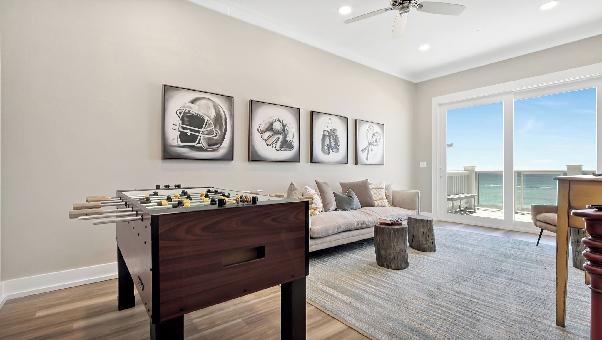 A spacious living room with a foosball table, a sofa, and a large window offering a view of the ocean.