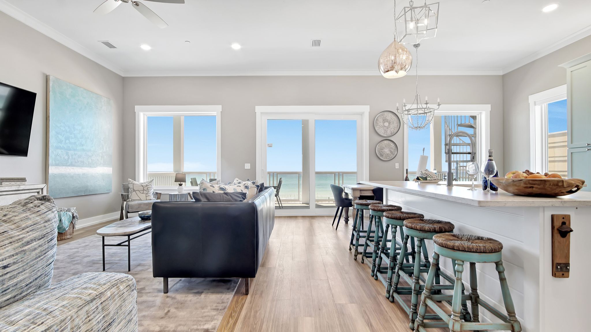 A spacious living room with a black sofa, a coffee table, and a TV. There is a large window with a view of the ocean.