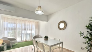 Een moderne eetruimte met een witte tafel en stoelen, een hanglamp, een grote spiegel en een potplant.