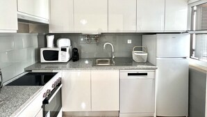 Een moderne keuken met witte kasten, een magnetron, een koffiezetapparaat, een spoelbak en een koelkast.