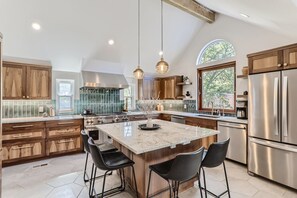 Una cocina amplia con una isla grande, armarios de madera, electrodomésticos de acero inoxidable y un ventanal que proporciona luz natural.