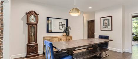 A dining area with a wooden table, blue upholstered chairs, a large wall clock, and a pendant light.