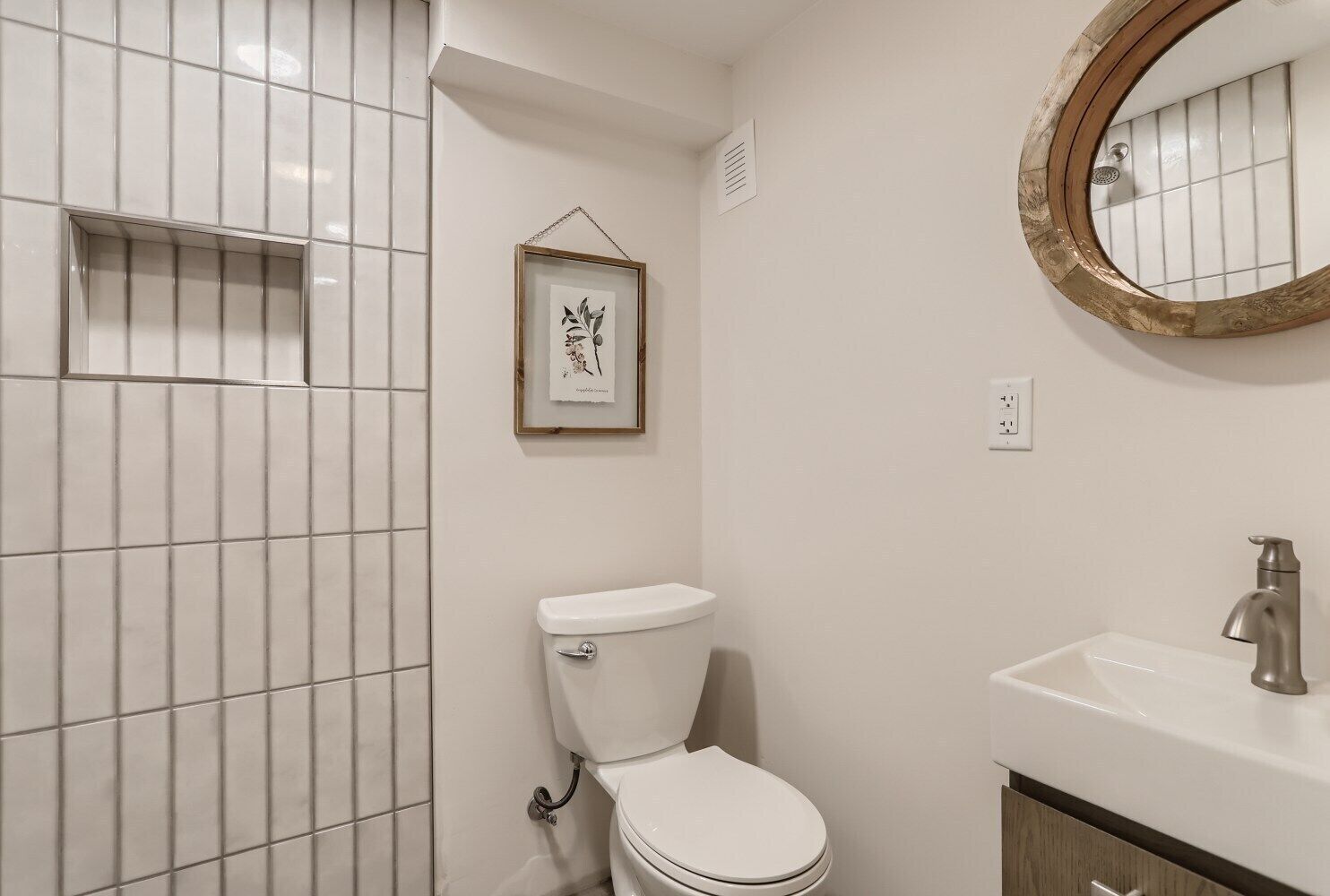 Ein Badezimmer mit Toilette, Waschbecken und einem gerahmten Pflanzenbild an der Wand.