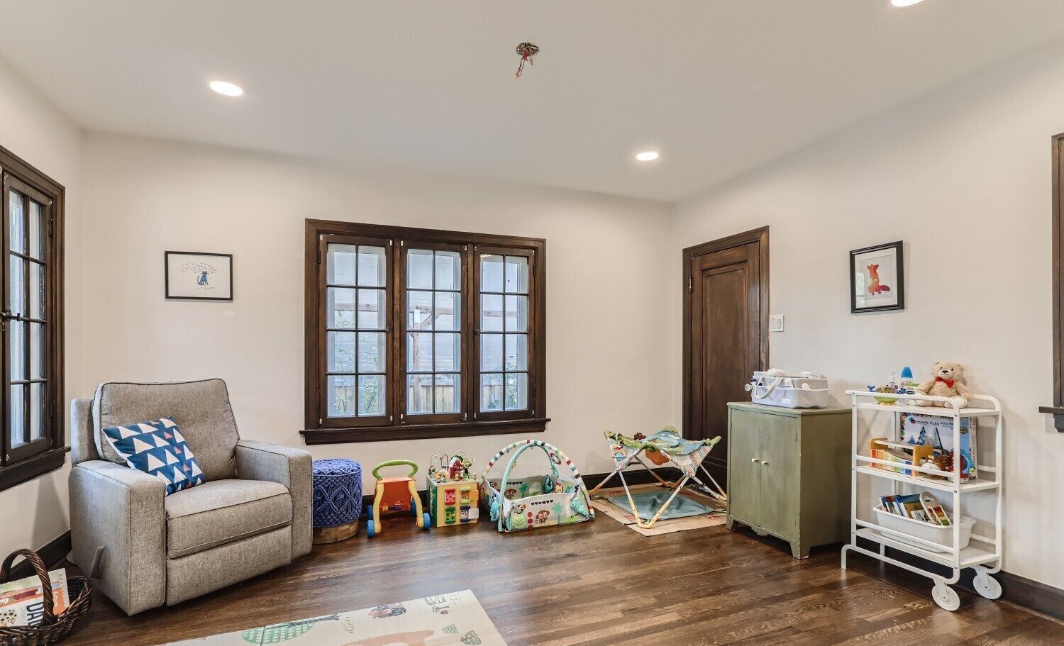 A cozy room with a grey armchair, a wooden cabinet, and a white shelf unit with toys.