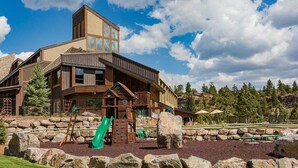 A lodge with a wooden exterior, a play area with a slide, and a view of the surrounding mountains. - Summit Style | AC, Pool, Hot Tub, Golf & Ski (Durango)