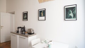 A small kitchenette with a coffee maker, toaster, and a white table with a chair. There are framed pictures on the wall. - Artsy and Elegant Apartment near Pantheon (Roma)