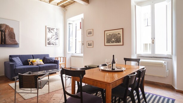 A dining area with a wooden table, chairs, a blue sofa, and artwork on the walls. - Artsy and Elegant Apartment near Pantheon (Roma)