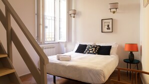 A bedroom with a bed, a window, a staircase, and a wall-mounted lamp. - Artsy and Elegant Apartment near Pantheon (Roma)