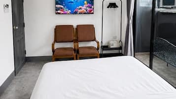 A hotel room with a bed, two chairs, a painting, an air conditioner, and a view of the outside.