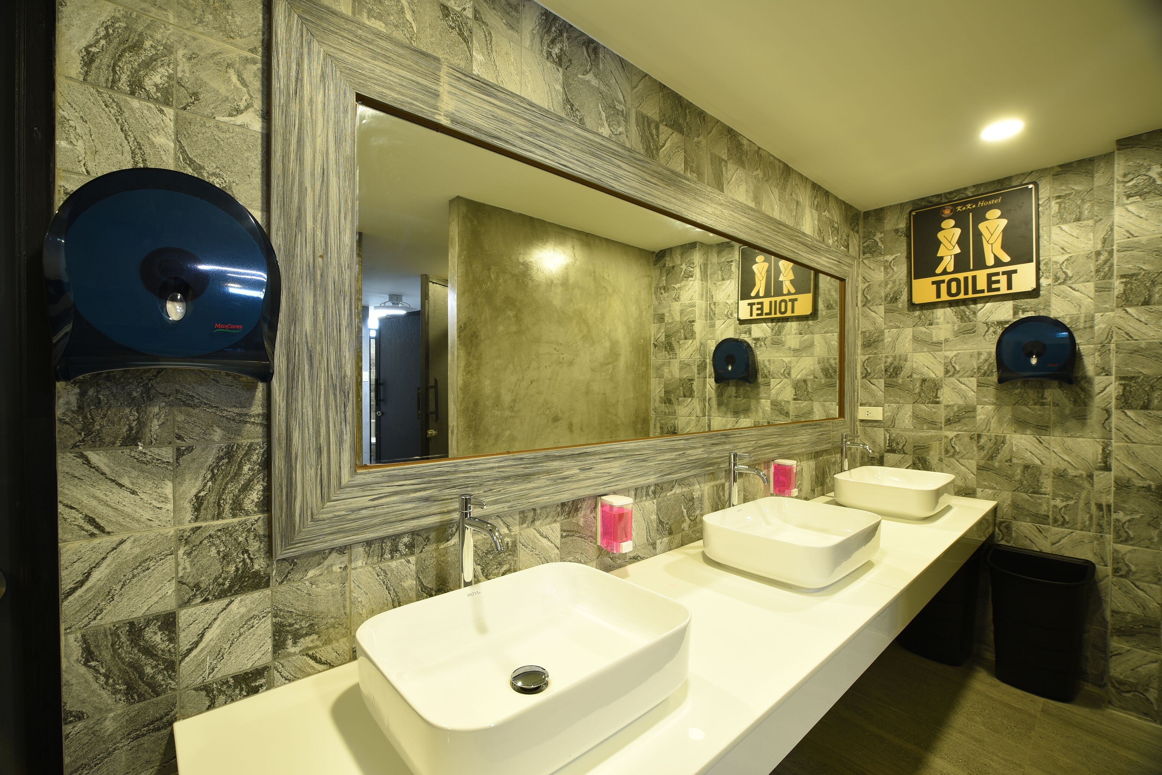 A modern bathroom with marble walls, three sinks, a large mirror, and a toilet sign.