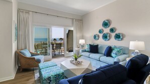 Una sala de estar con un sofá azul claro, un sillón de mimbre, una mesa de centro y vista al océano a través de una puerta corrediza de vidrio.