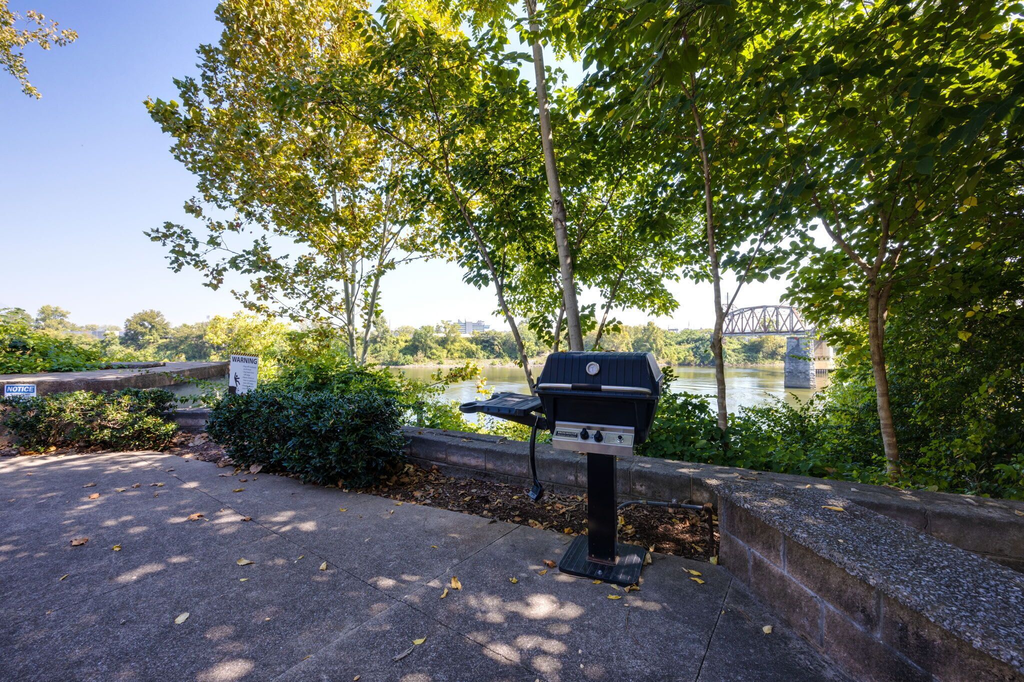 Un barbecue installé dans un parc, avec une rivière et un pont en arrière-plan.