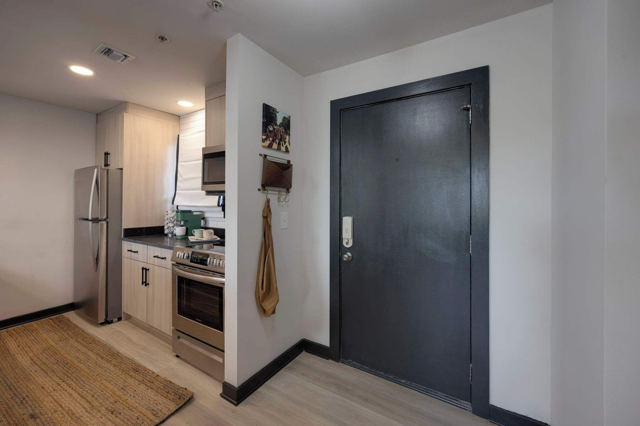 Una cocina moderna con electrodomésticos de acero inoxidable, microondas y cafetera. Hay una puerta con manija y un estante pequeño arriba.