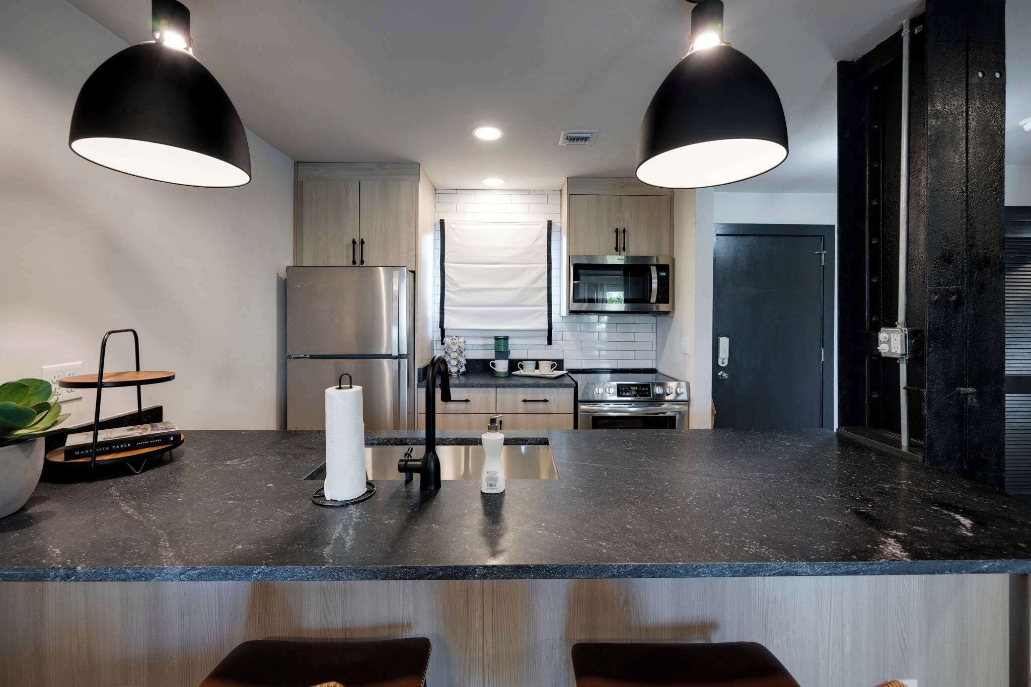 Una cocina moderna con encimera negra, electrodomésticos de acero inoxidable e iluminación colgante.