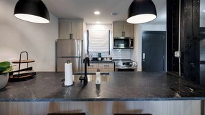 A modern kitchen with a black countertop, stainless steel appliances, and pendant lighting.