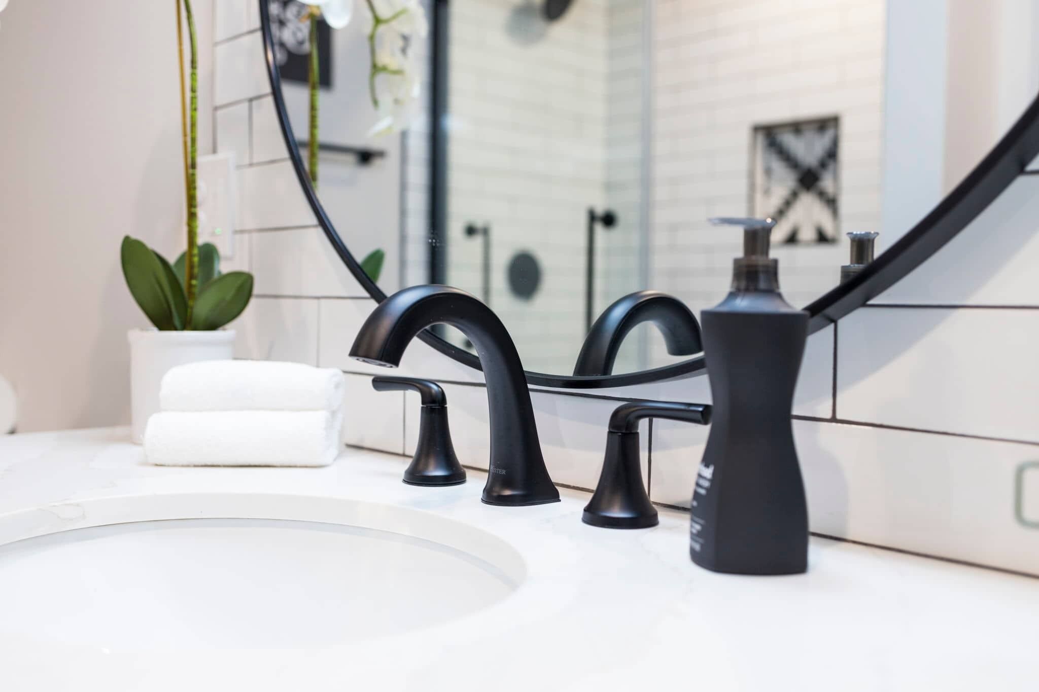 A modern bathroom with a white sink, black faucets, and a potted plant.
