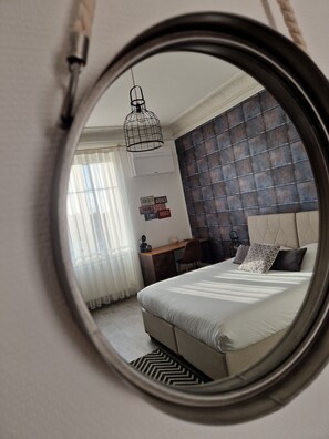 A bedroom with a round mirror reflecting the room. It includes a bed, a desk, and a chair. - Hipster Suites - Chez Axelle (Colmar)