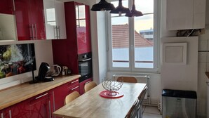 A modern kitchen with red and white cabinets, a wooden dining table, and a view of the outside through a window. - Hipster Suites - Chez Axelle (Colmar)