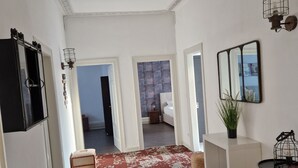 A hallway with a patterned carpet, a brown chair, a white console table, and a black barrel. - Hipster Suites - Chez Axelle (Colmar)