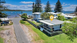 A coastal property with a large house featuring a balcony, a smaller attached structure, and a view of the sea. - Sunset Sails Taylors Beach NSW (Taylors Beach)