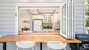 A modern kitchen with a wooden table and white chairs, a refrigerator, and a stove. - Sunset Sails Taylors Beach NSW (Taylors Beach)
