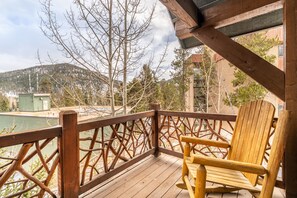A wooden deck with a wooden chair, overlooking a mountainous landscape and a body of water.