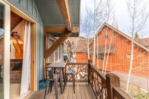 A wooden deck with a table and chairs, a staircase leading to an upper level, and a view of a red wooden building in the background. - Private Balconies and Huge Windows for Gorgeous Mountain Views! (Keystone)